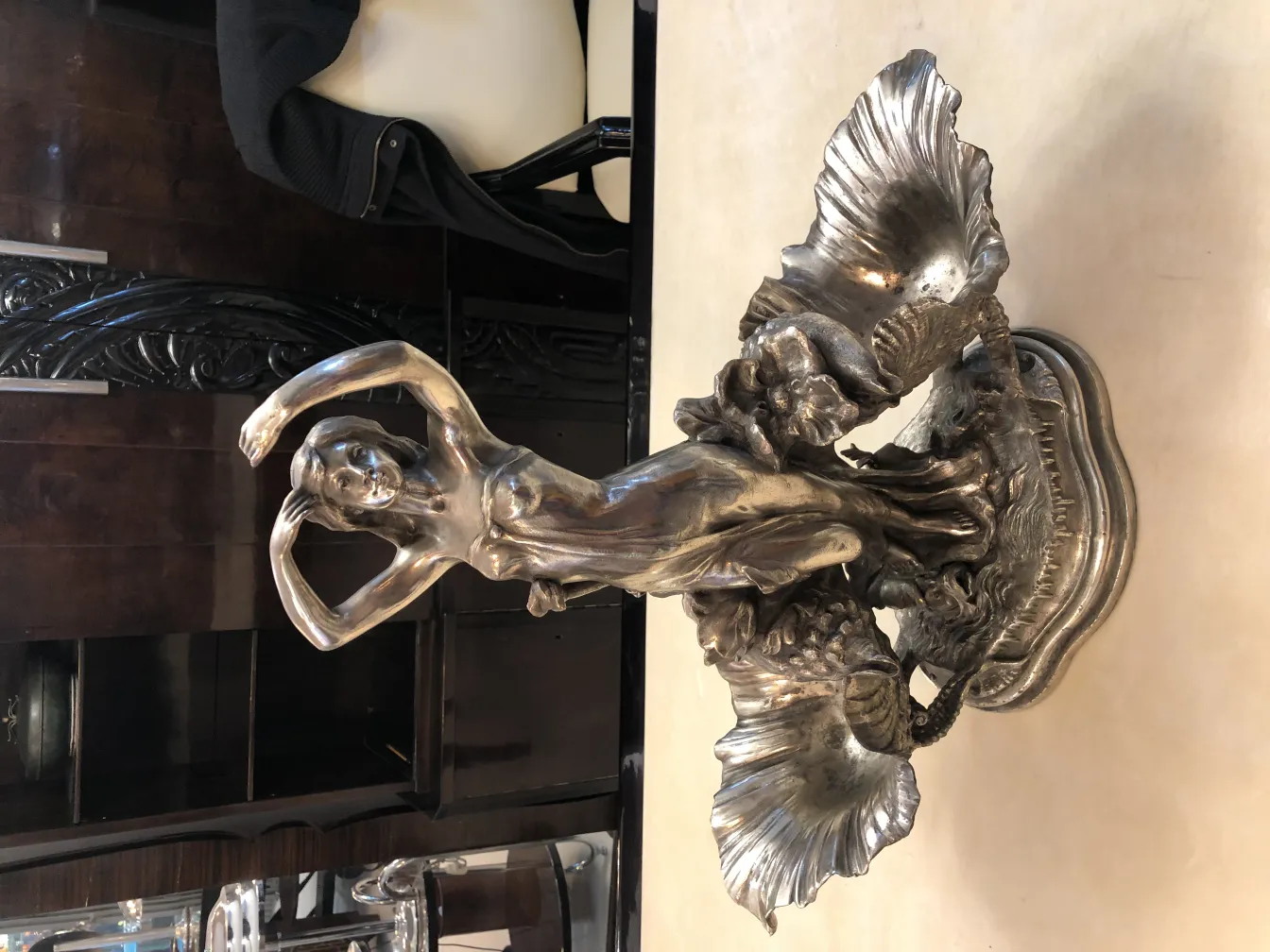 Centre de table ancien avec figure féminine parmi des coquilles décoratives, sur fond sombre.