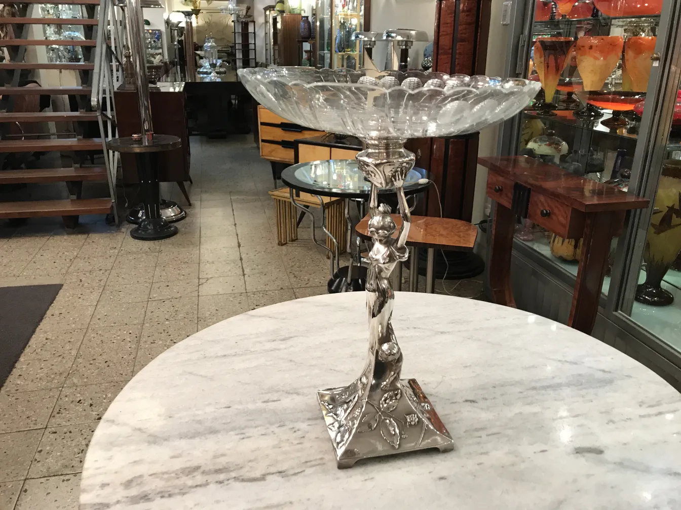 Centro de mesa antigo WMF em forma decorativa com base elaborada, cercado por um ambiente aconchegante.