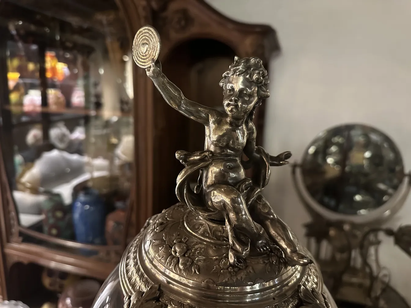 centrotavola wmfs a forma di figura decorativa di bambino che tiene un disco, sullo sfondo altri oggetti d'antiquariato