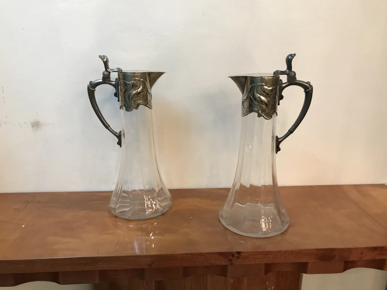 Duas jarras de estilo antigo com detalhes elegantes, em uma mesa de madeira.