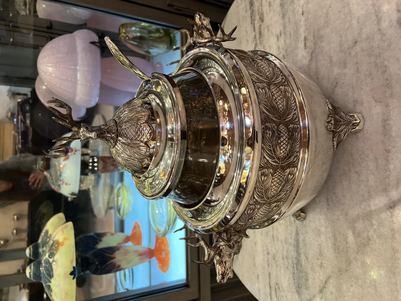 Antique WMF punch bowl with relief details and deer-shaped lid, surrounded by other antiques.
