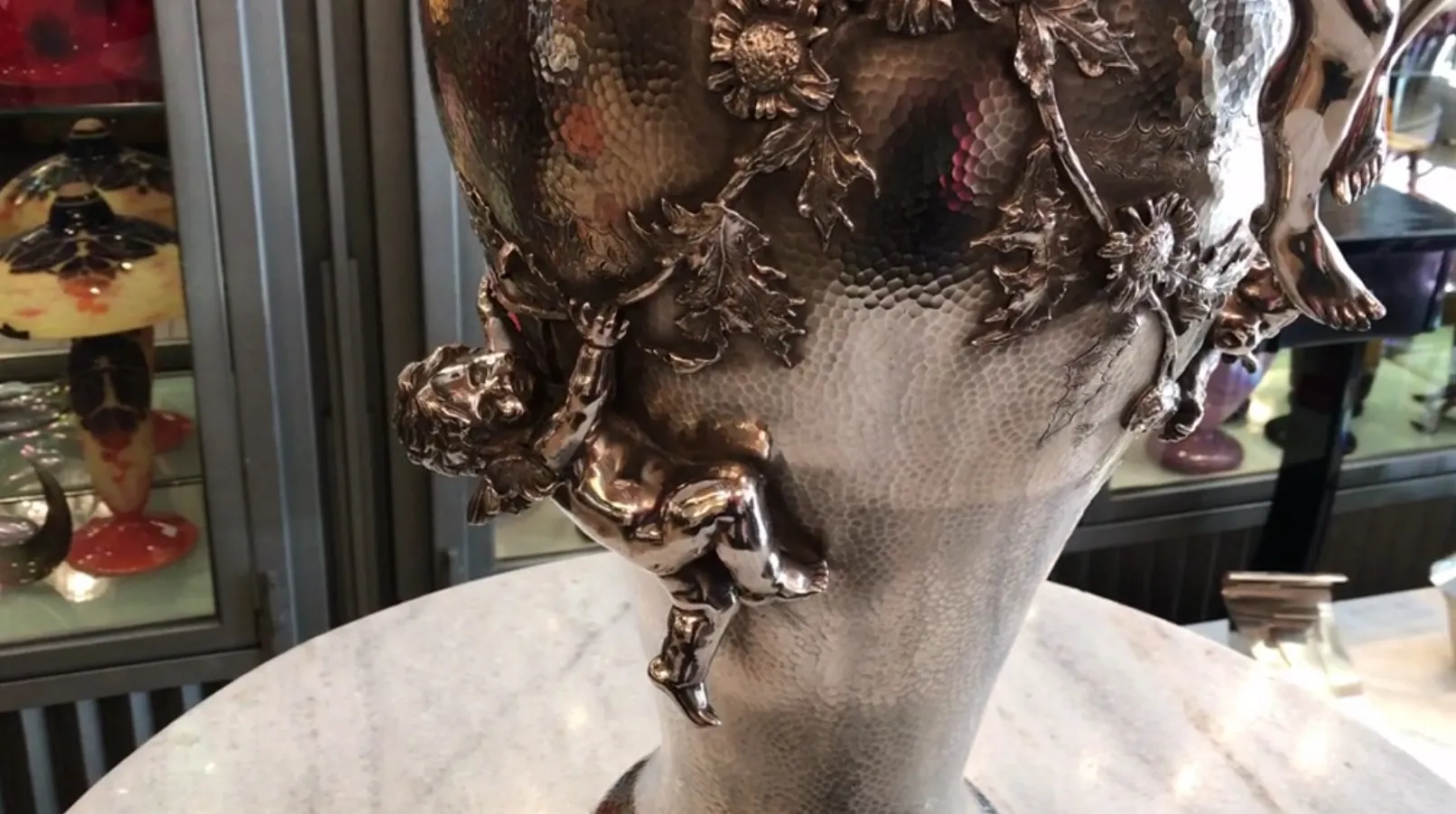 vaso antico Orivit con un cherubino che tiene fiori, decorato con foglie e fiori.