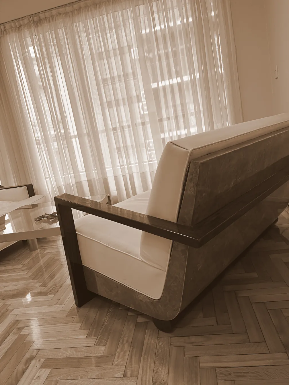 Poltrona antiga com design elegante e limpo, em uma sala iluminada com grandes janelas.