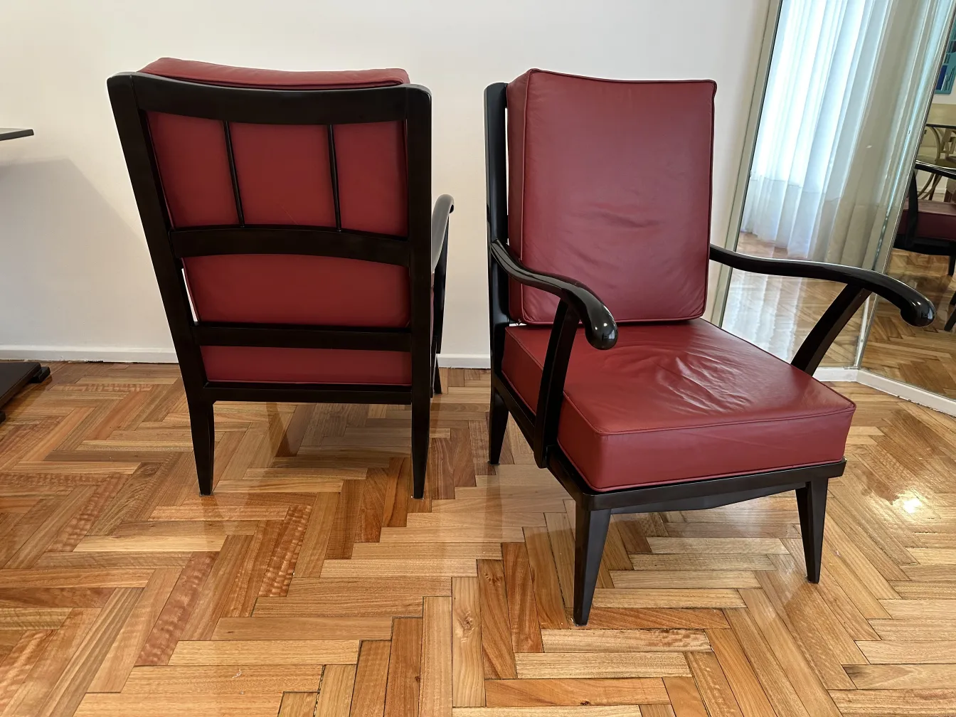 Conjunto de 2 sillones antigüedades elegantes con tapizado en color burdeos, con patas rectas y brazos en curva, sobre un suelo de madera clara.
