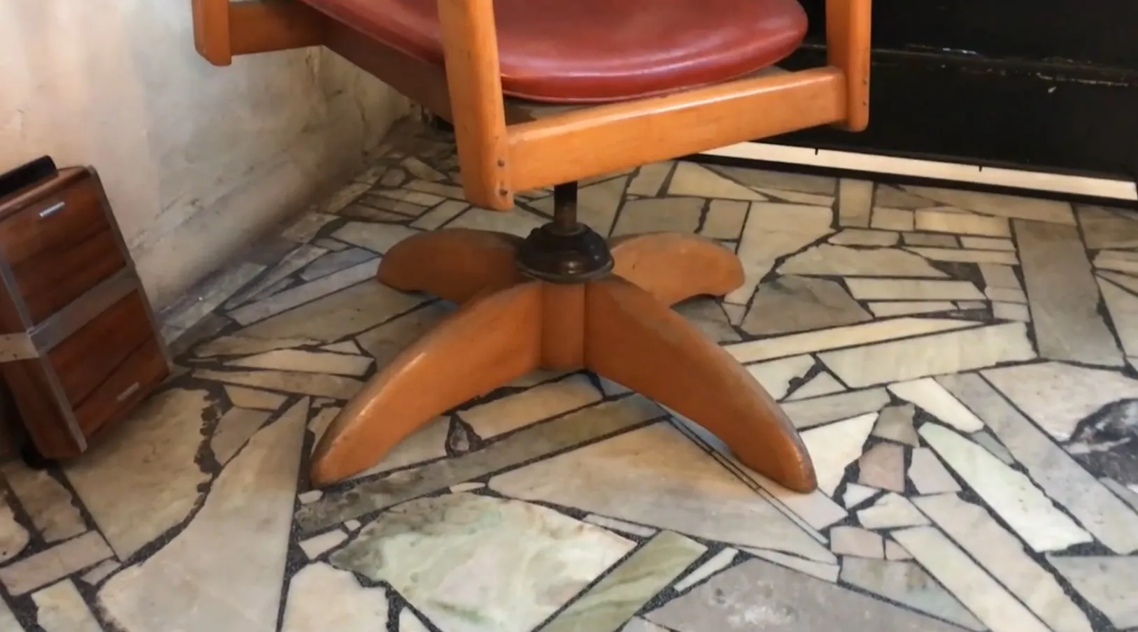 पुरानी कार्यालय कुर्सी साधारण और कार्यात्मक डिजाइन के साथ, घूर्णन आधार और लाल अस्तर, आरामदायक वातावरण में स्थित है।