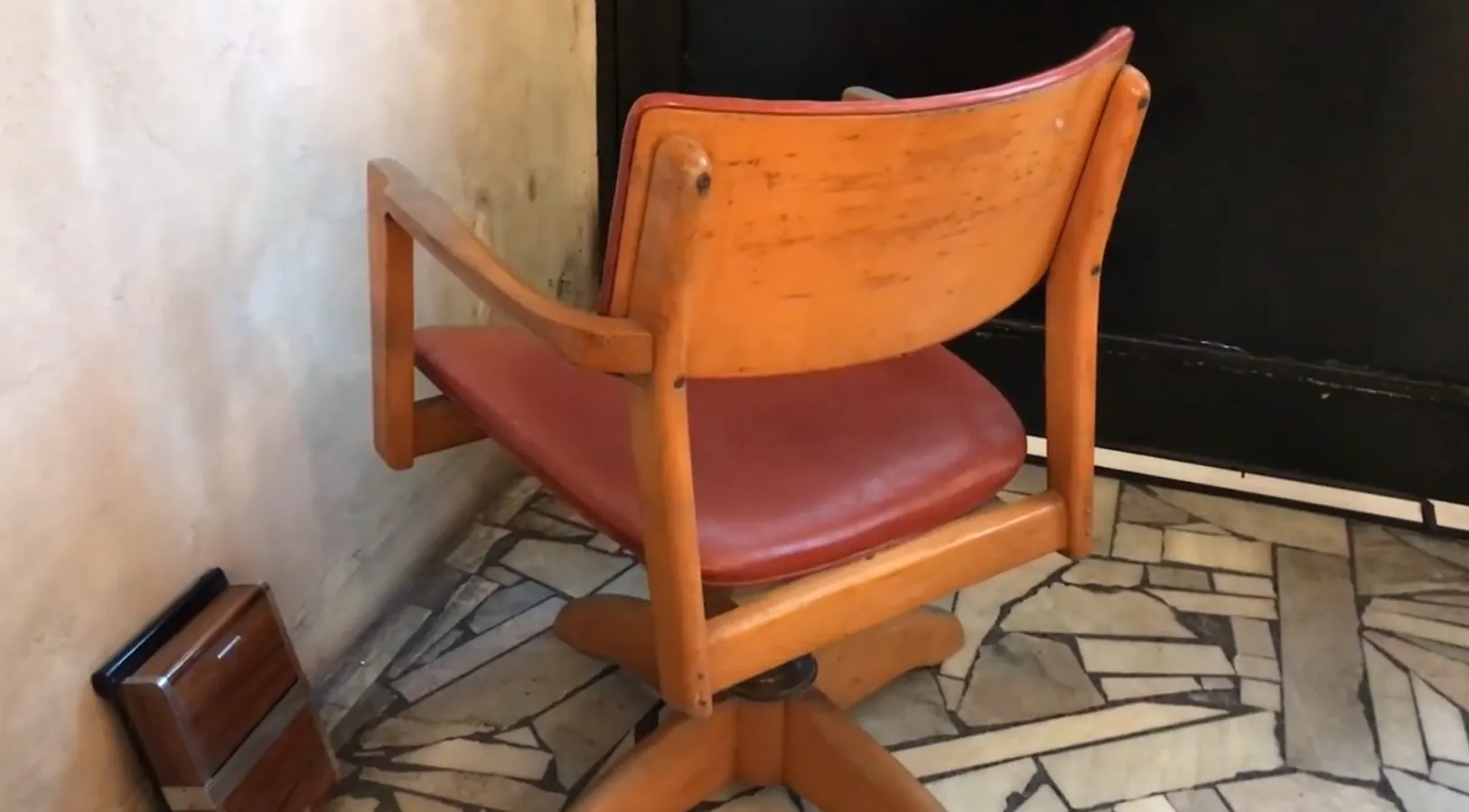 Sillón de escritorio antiguo con brazos y asiento rojo, ambiente relajado.
