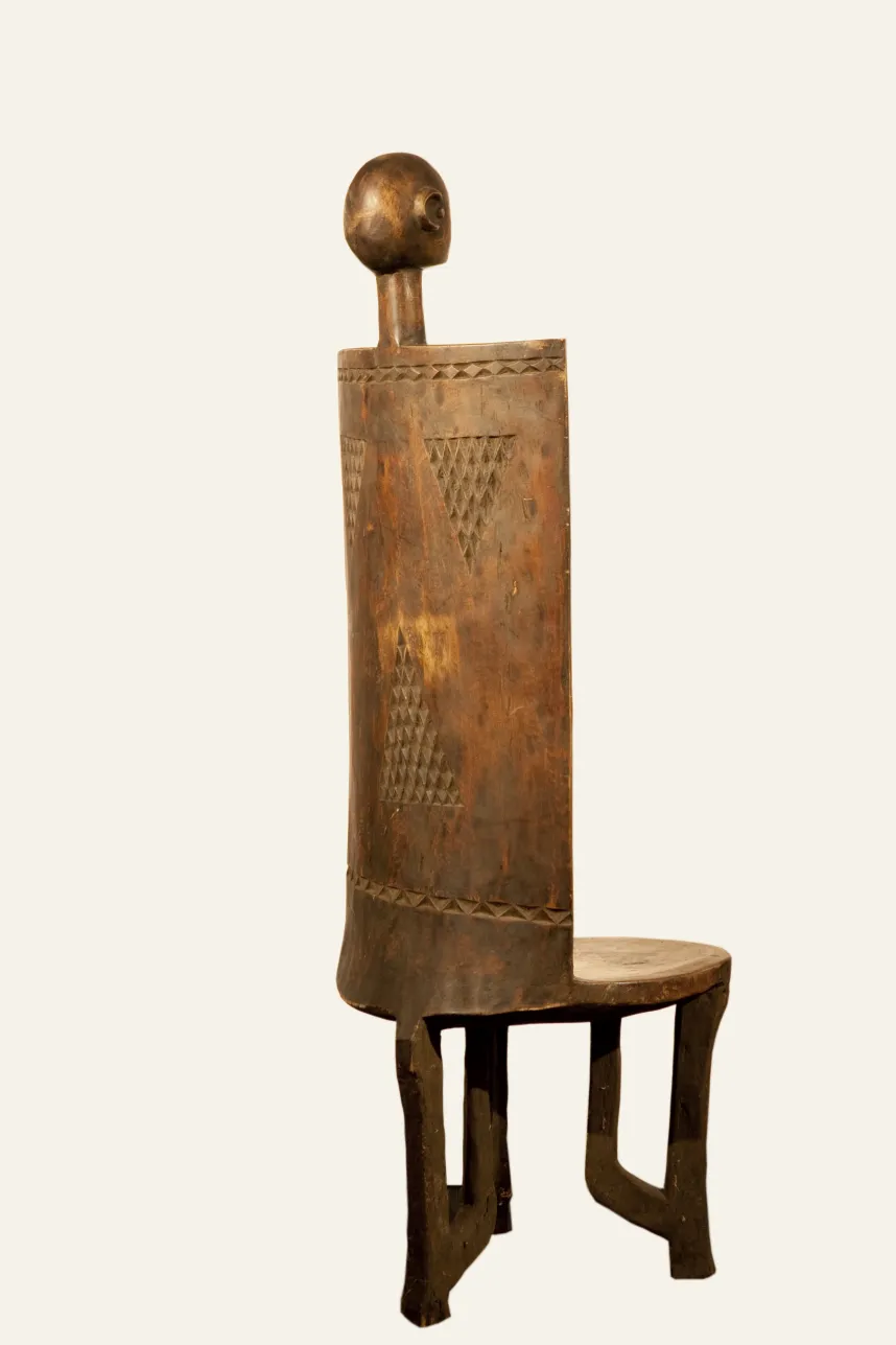Antique chair with a backrest and figure on top, tribal design visible.