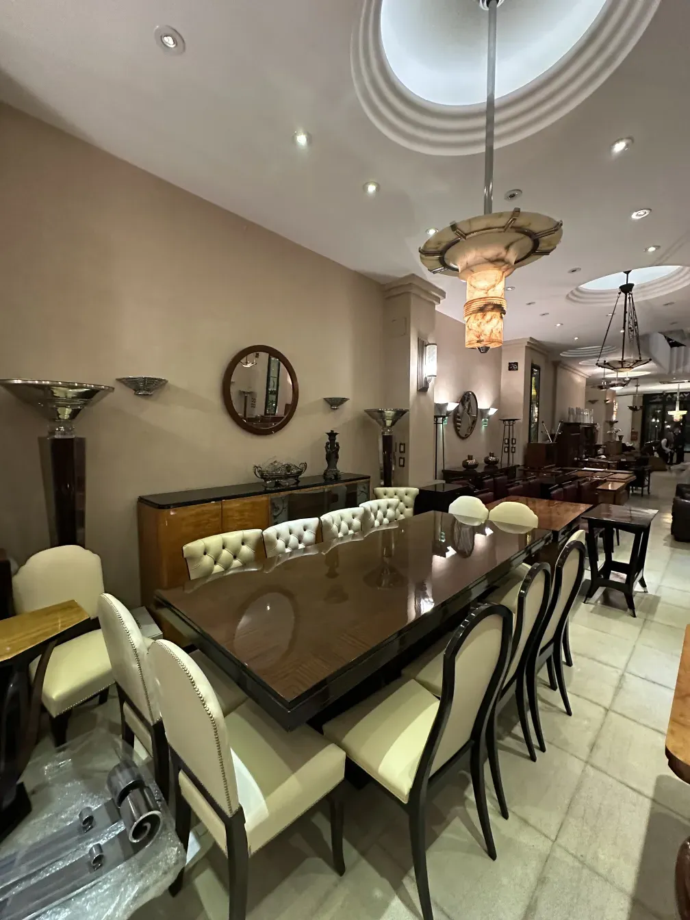 Doze cadeiras antigas elegantes ao redor de uma grande mesa, decoradas com estofados claros.