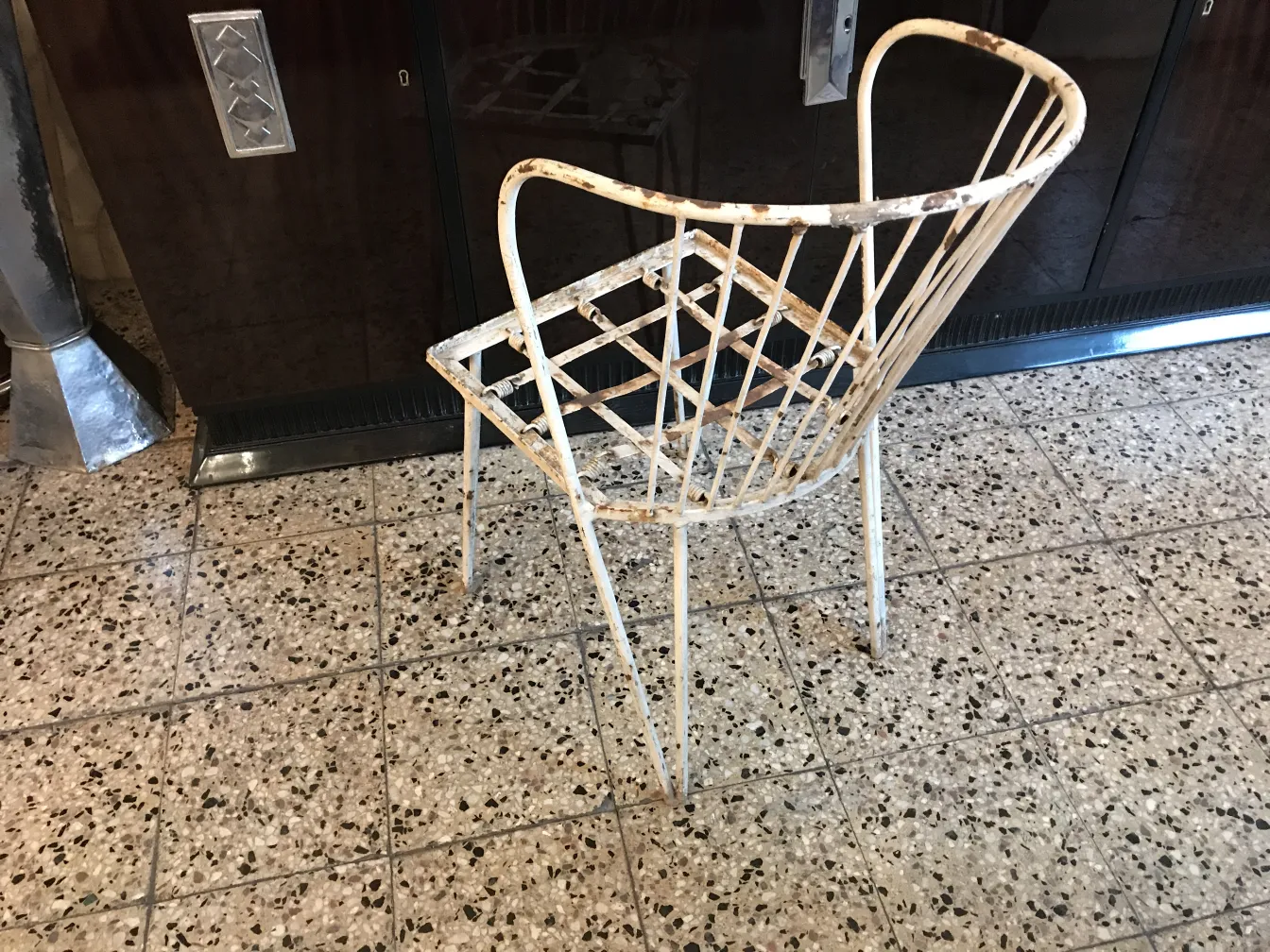 Cadeira de jardim antiga com design de treliça e desgaste visível, de cor clara.