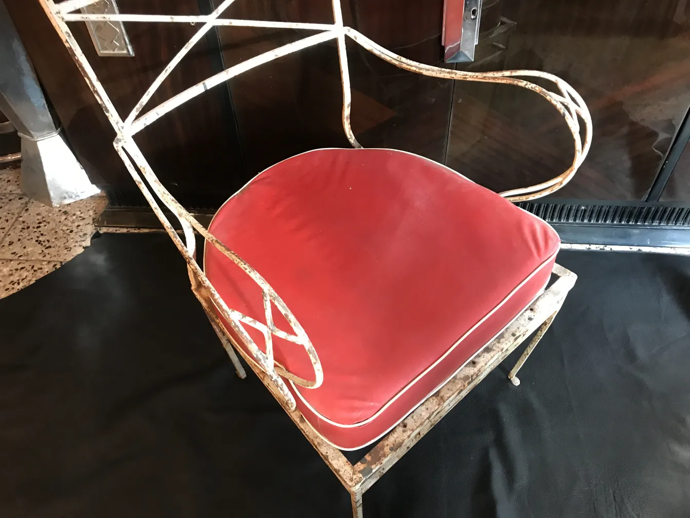 Fauteuil de jardin ancien avec coussin rouge dans un cadre élégant.