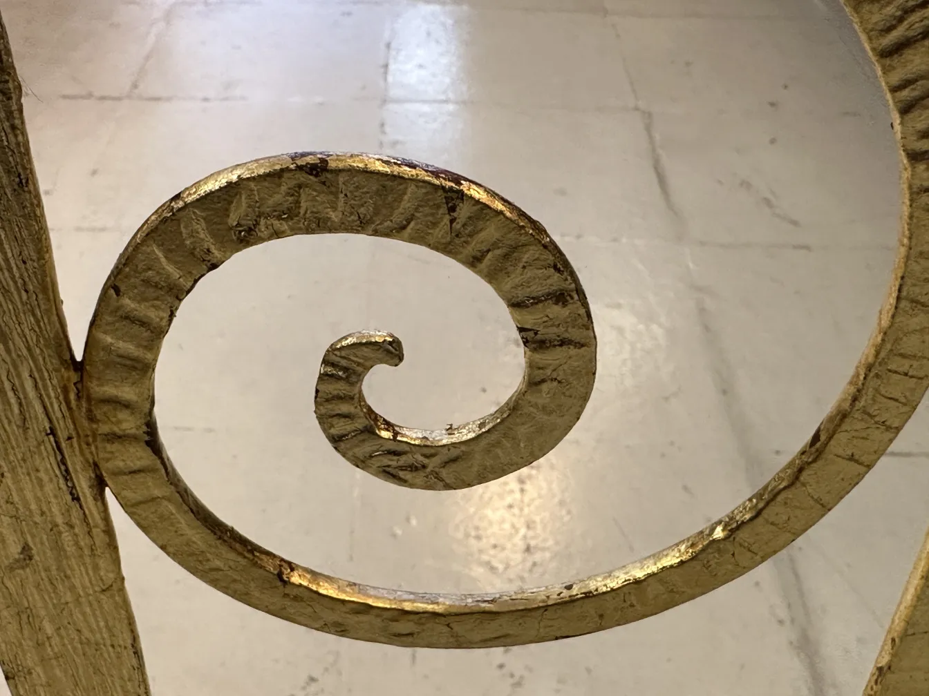 Detail of an antique umbrella stand with golden spiral design on a light background.