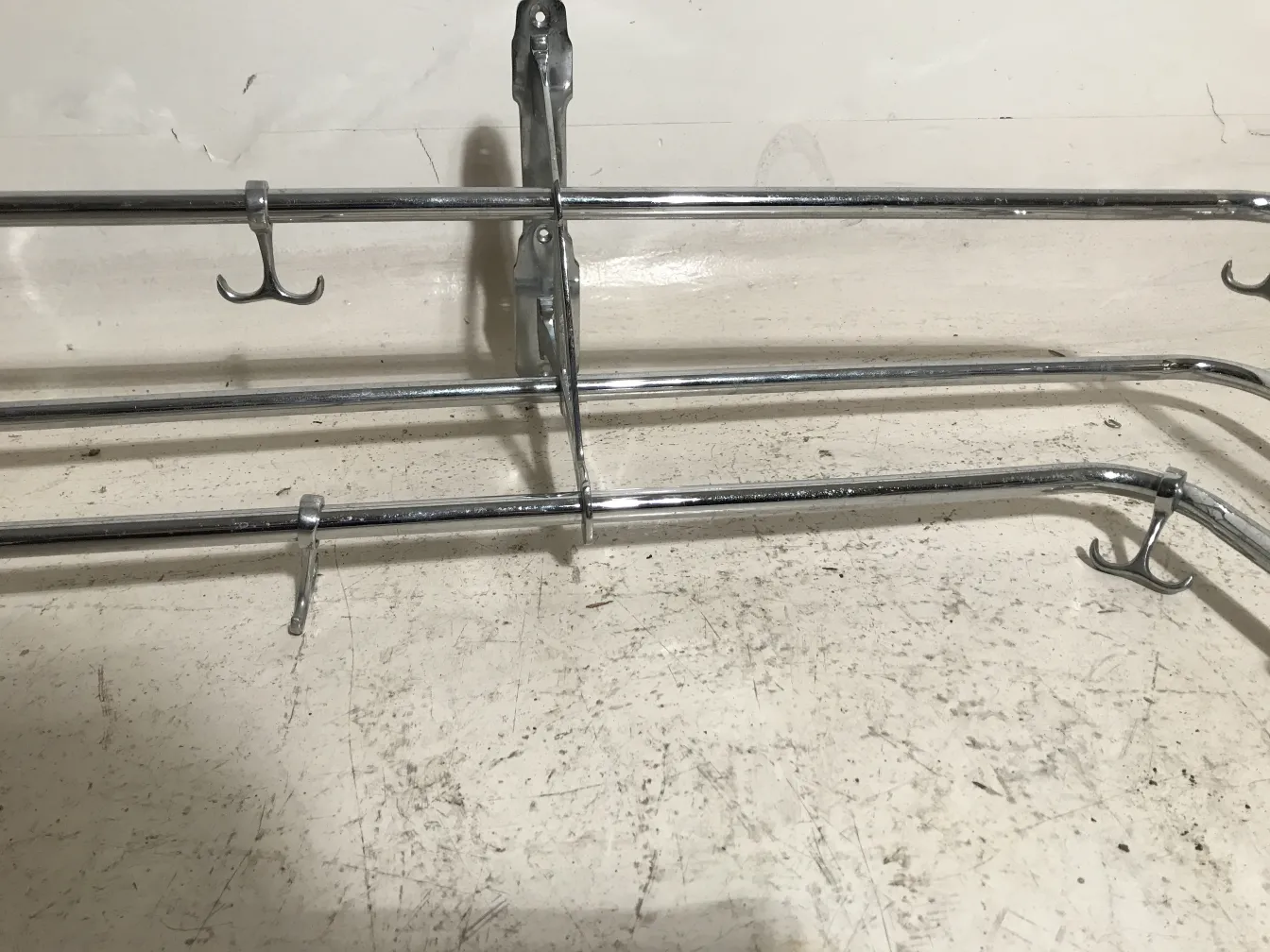 Perchero antiguo con estructura metálica y varios ganchos en un entorno neutro.