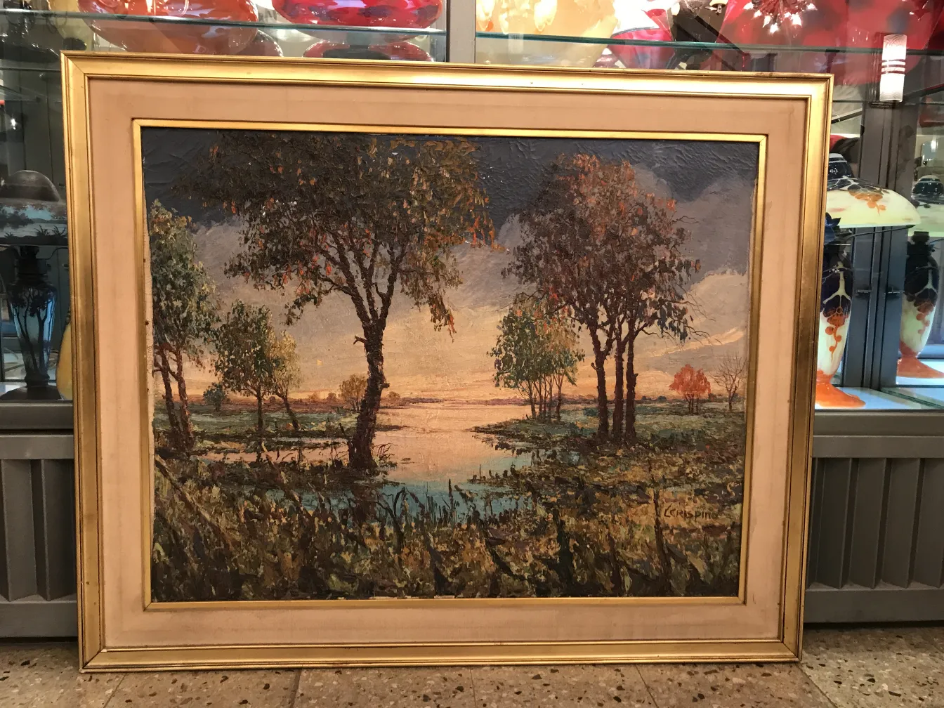 Pintura Crispino de uma paisagem com árvores e água em uma moldura dourada.