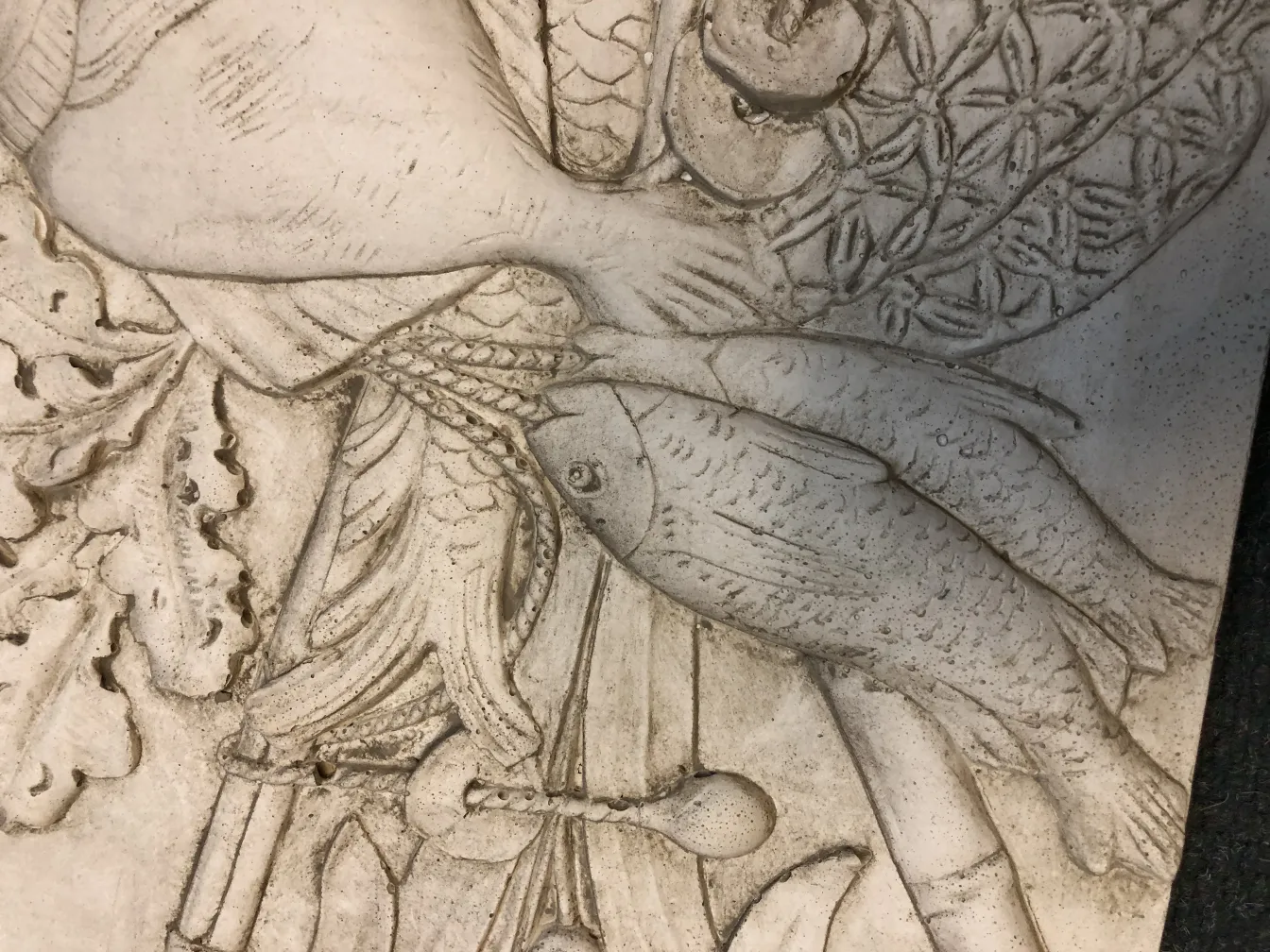 Antique wall plate featuring a relief design of fish and ornamental details.