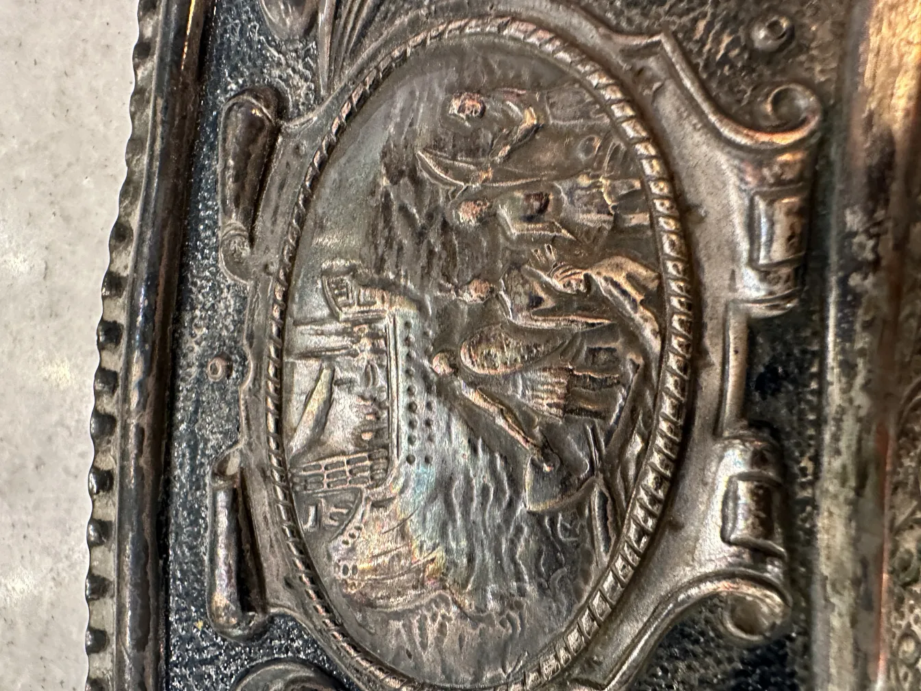 Placa de parede antiga representando uma cena marinha com barcos e figuras.