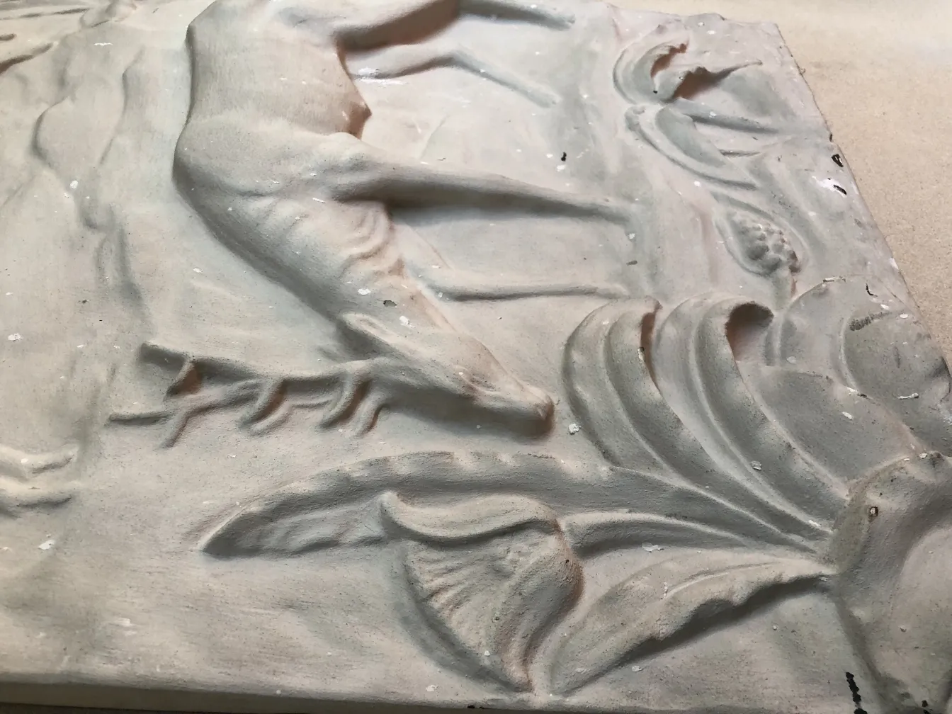 Plaque murale ancienne avec relief de fleurs et feuilles sur un fond clair.