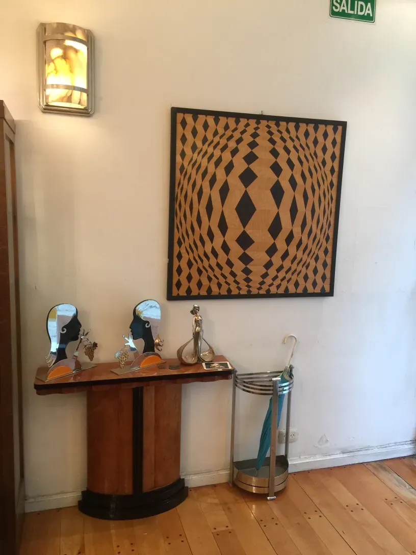 Marqueterie ancienne sur un mur blanc, avec des formes géométriques en tons sombres et clairs, se démarquant dans un environnement accueillant.