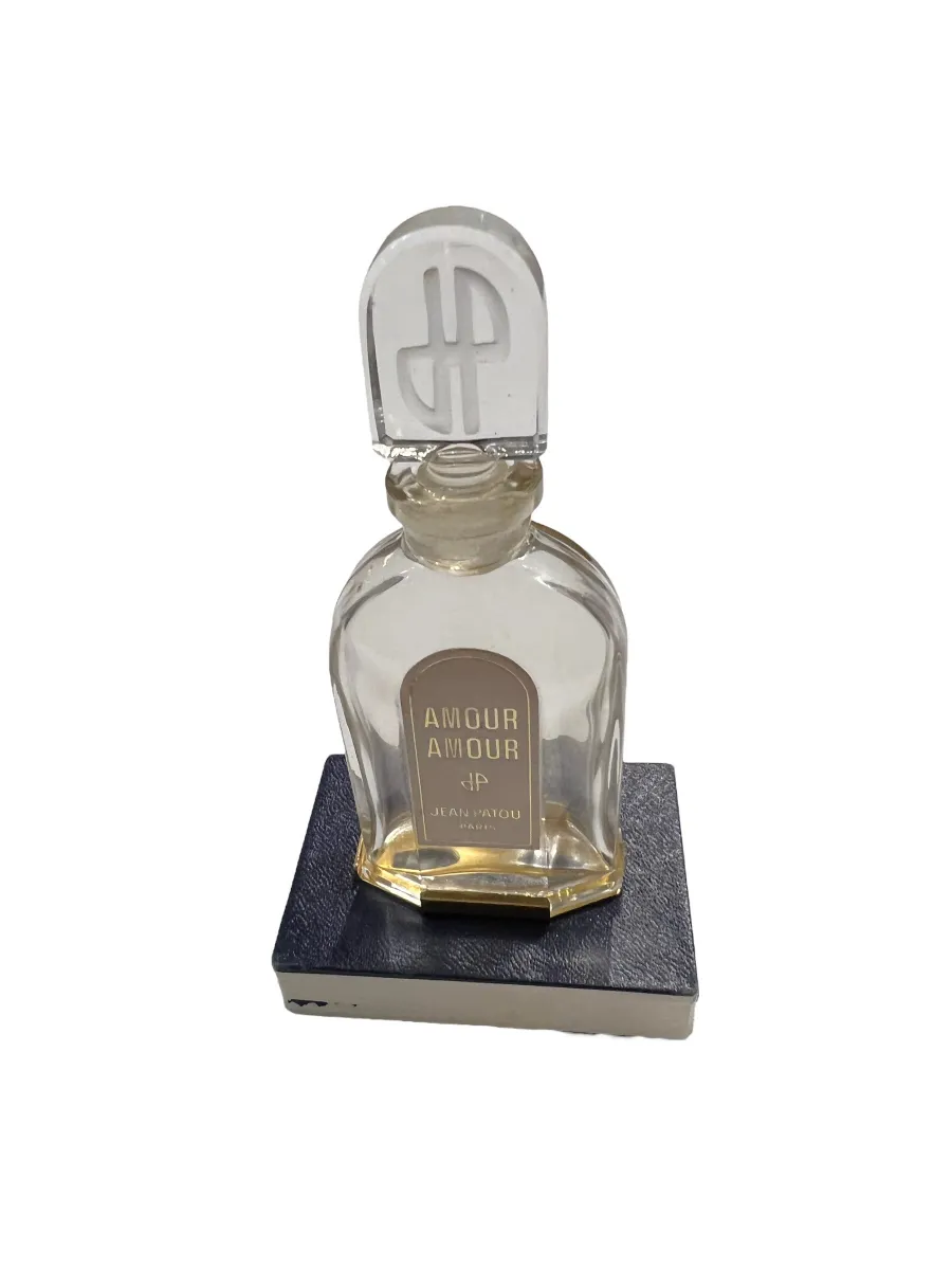 Frasco de perfume antiguo con tapa distintiva en forma de símbolo, decorado con la marca Jean Patou