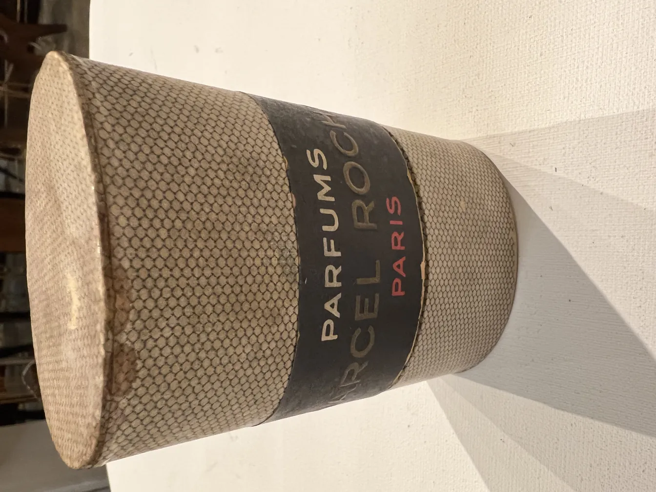 Flacon de parfum antique en forme cylindrique avec détails décoratifs, fond clair.