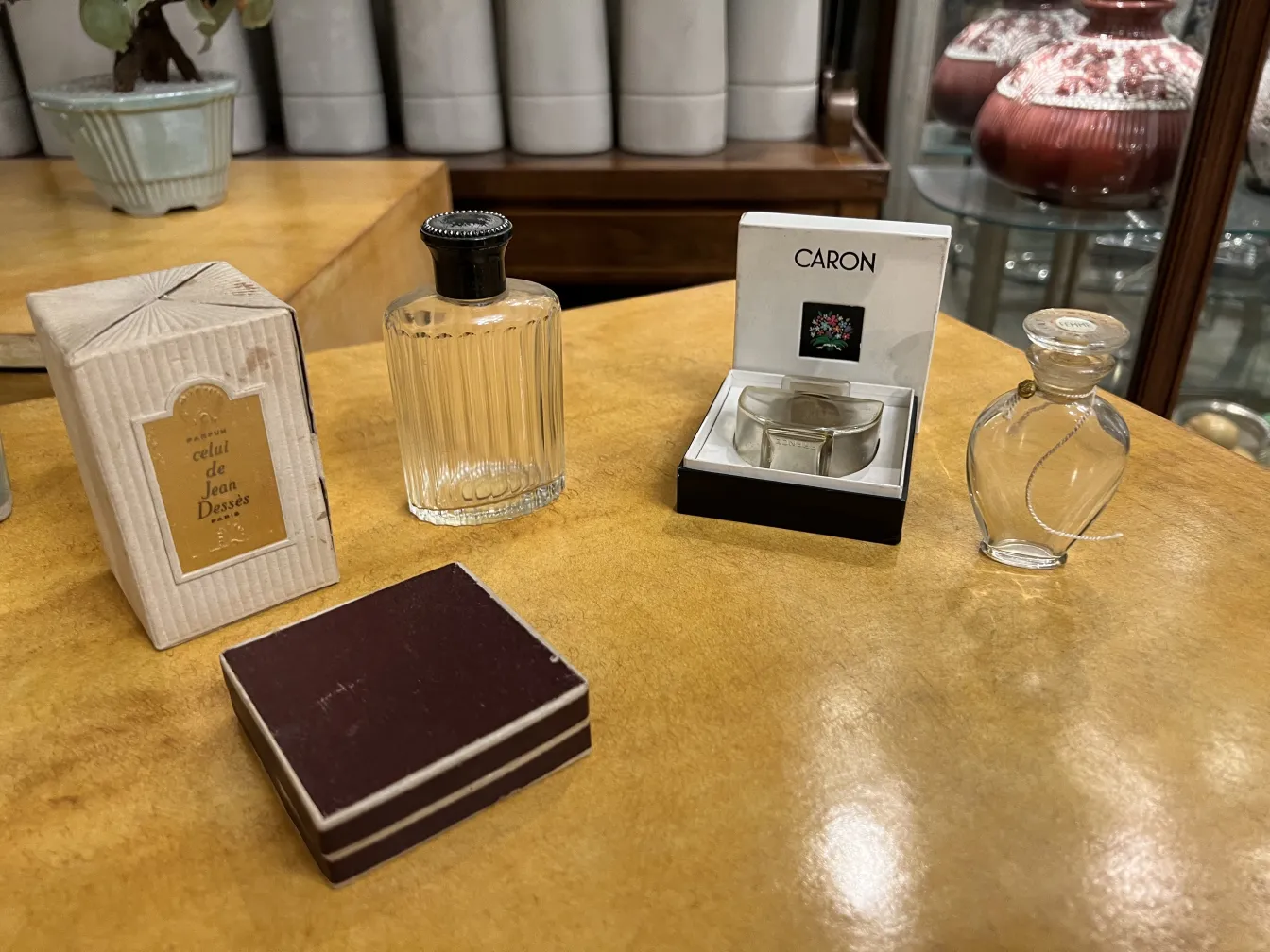 Flacone di profumo antico con tappo nero e forma arrotondata su sfondo giallo, con altri oggetti decorativi.