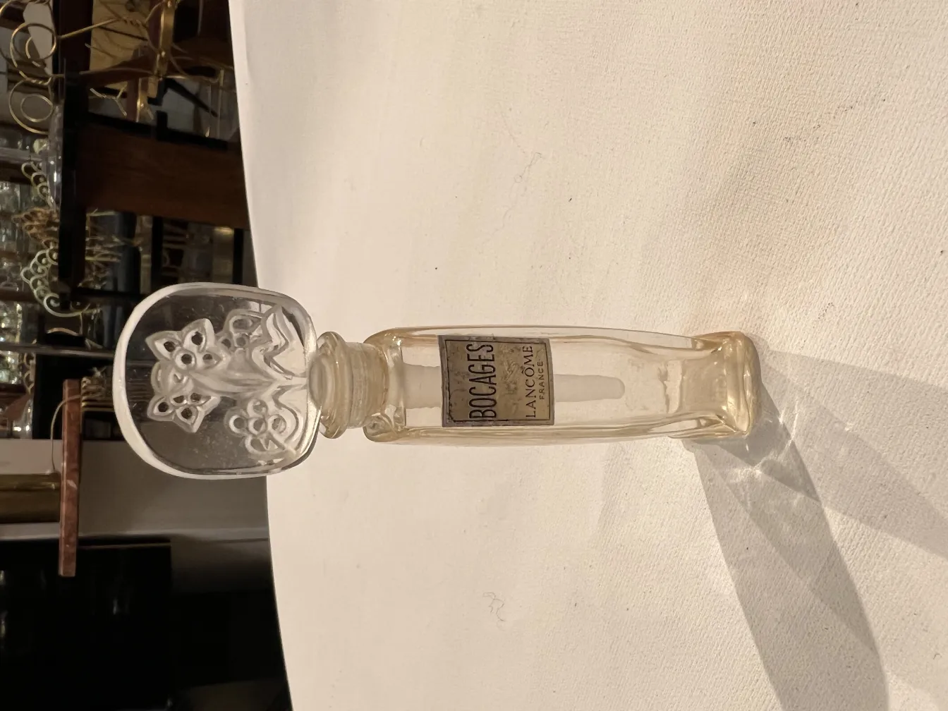 Flacon de parfum ancien avec un capuchon floral, reflétant la lumière sur un fond doucement éclairé.