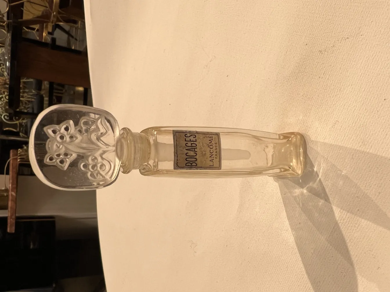 antique perfume bottle with decorative floral cap, reflections on a clear table