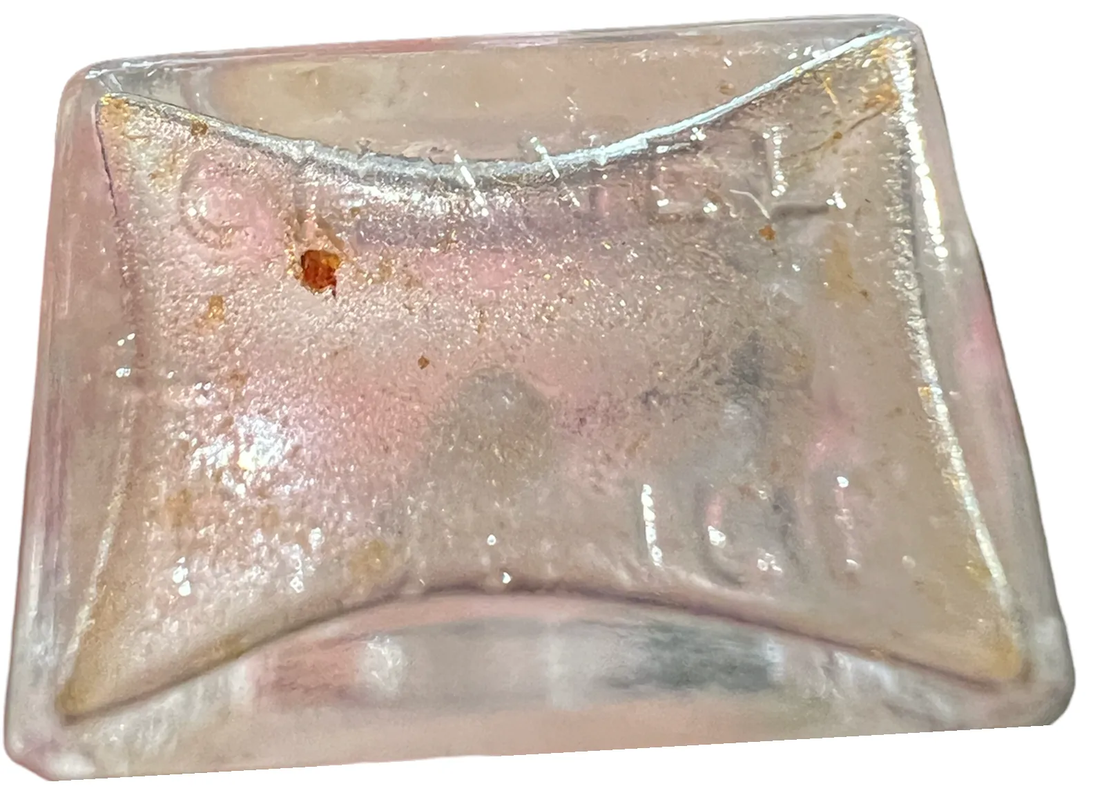 زجاجة عطر قديمة على شكل وسادة، مع تفاصيل تالفة وتصميم أنيق، تعكس الضوء بشكل خفيف.