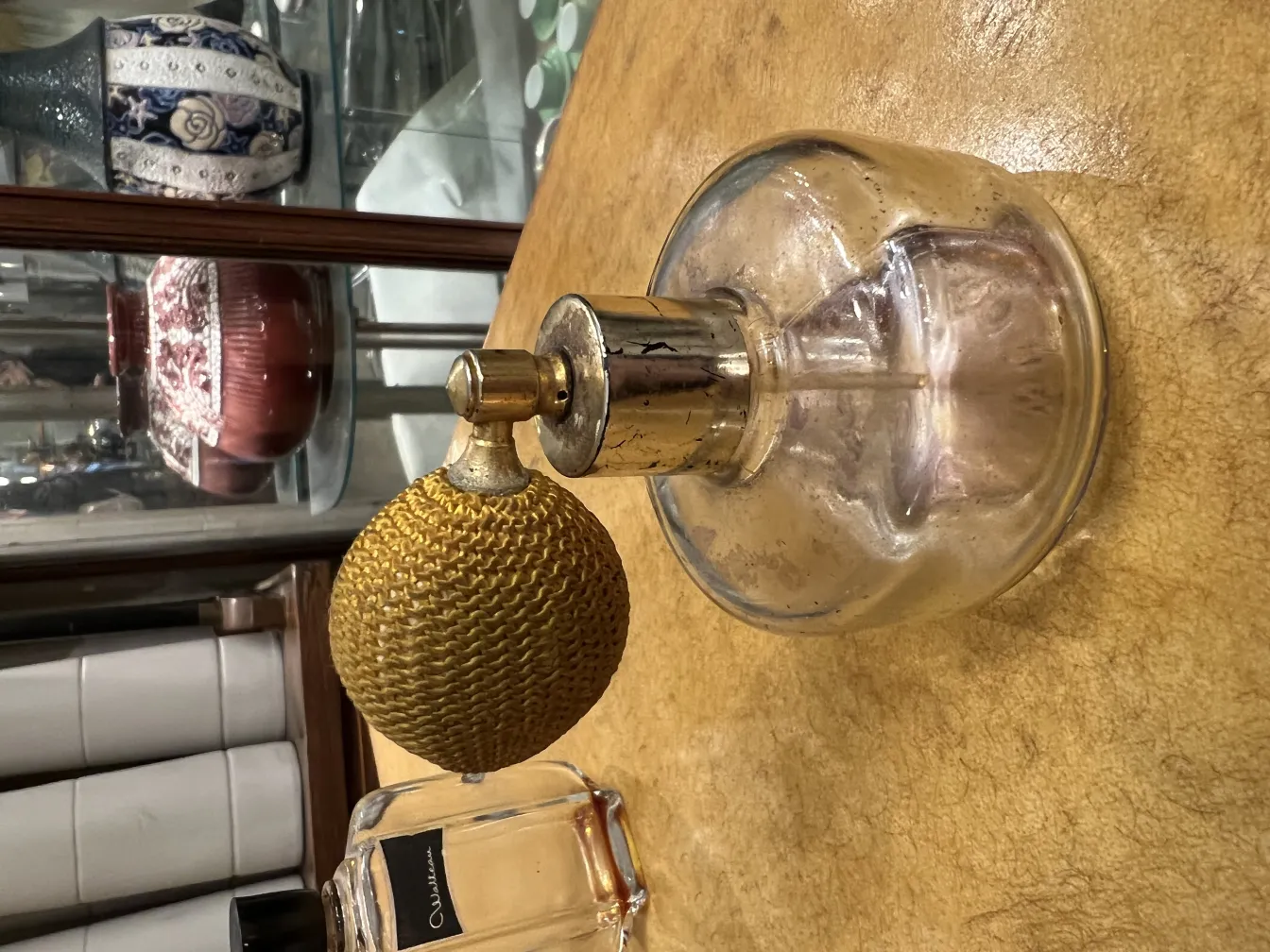 古董香水瓶，有金色球形喷雾器和透明底座，背景虚化的各种物品