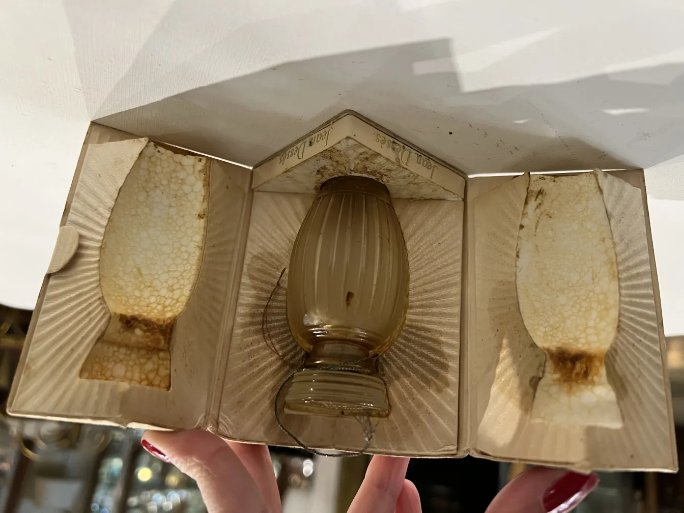 زجاجة عطر قديمة في علبة بها تفاصيل. لون فاتح وتصميم كلاسيكي.