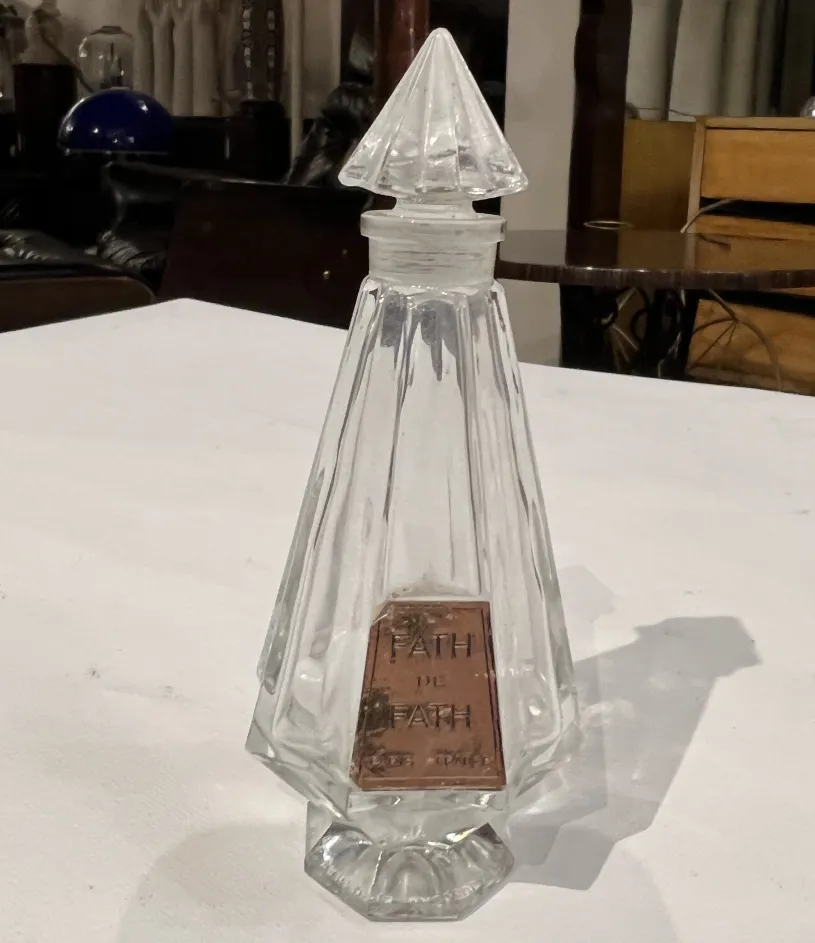 Flacone di profumo antico con forma rettangolare e coperchio a piramide, etichetta visibile.