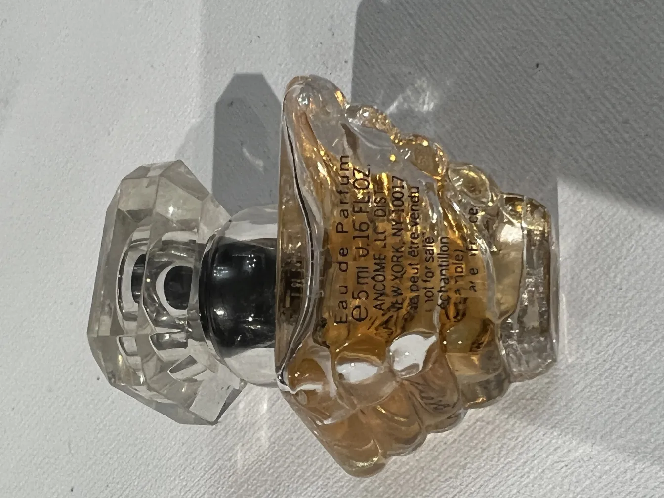 Flacone di profumo antico con coperchio facettato e liquido giallo.