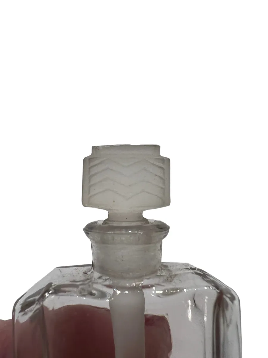 Frasco de perfume antigo com tampa decorativa, em um fundo claro.