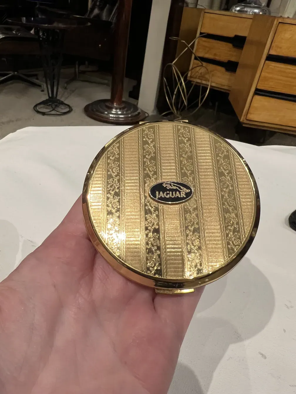 Polvera ancienne avec un design doré et le logo Jaguar Stratton sur fond clair.