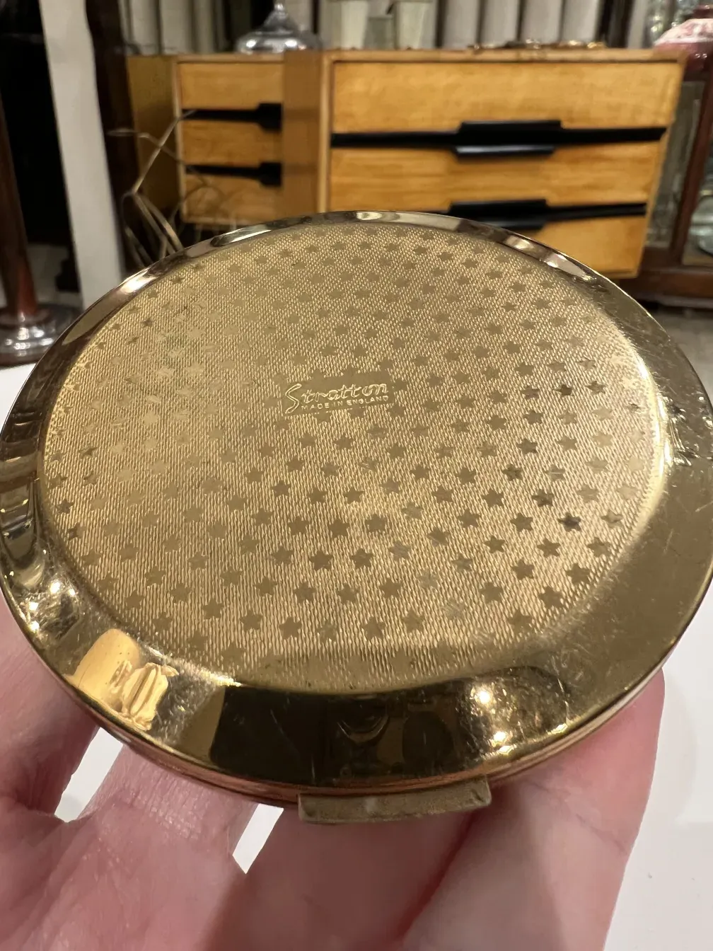 Polvera antigua Stratton England con diseño dorado, admirada en una mano.