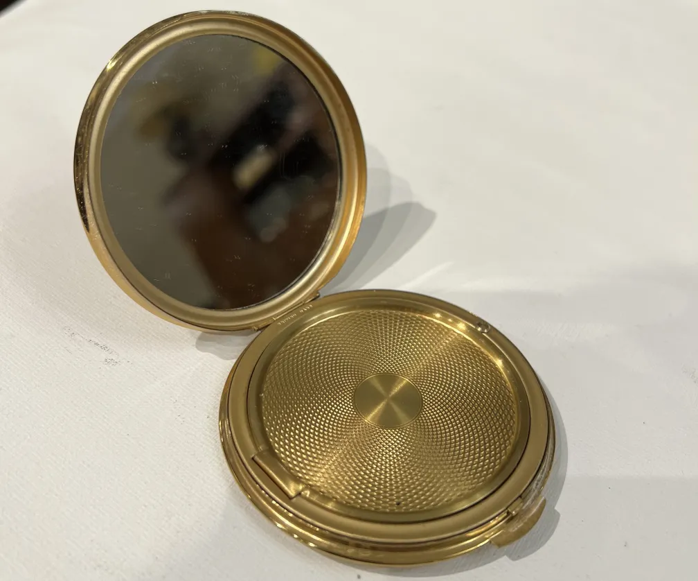 Polvera antiga apresentando um design dourado e um espelho interno.