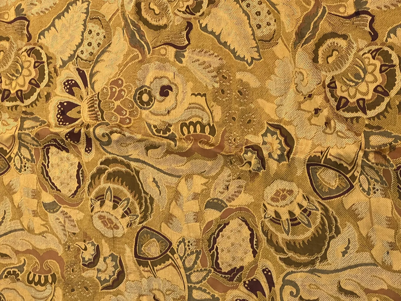 Antike Tischdecke mit floralen Mustern in goldenen und burgunderfarbenen Tönen, strukturierter Hintergrund.