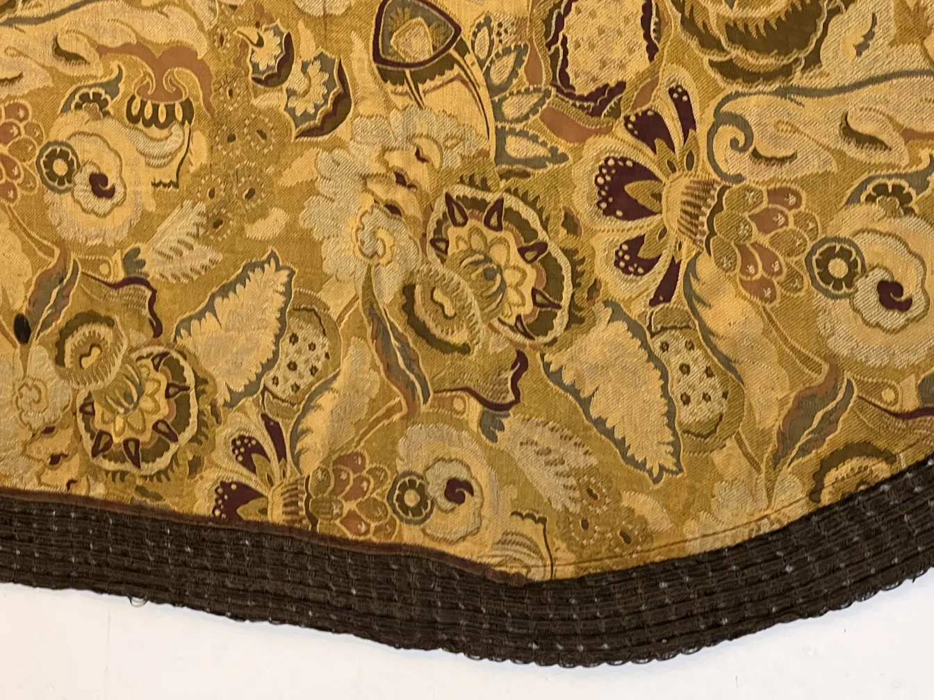 Toalha de mesa antiga com estampa floral colorida e borda contrastante, colocada em uma superfície branca.