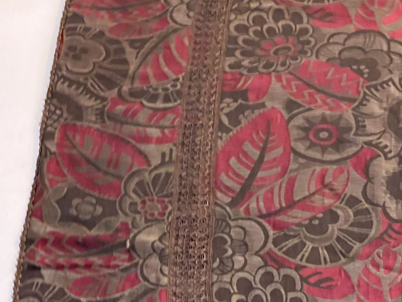 Antique tablecloth with red and gray flowers on a table.