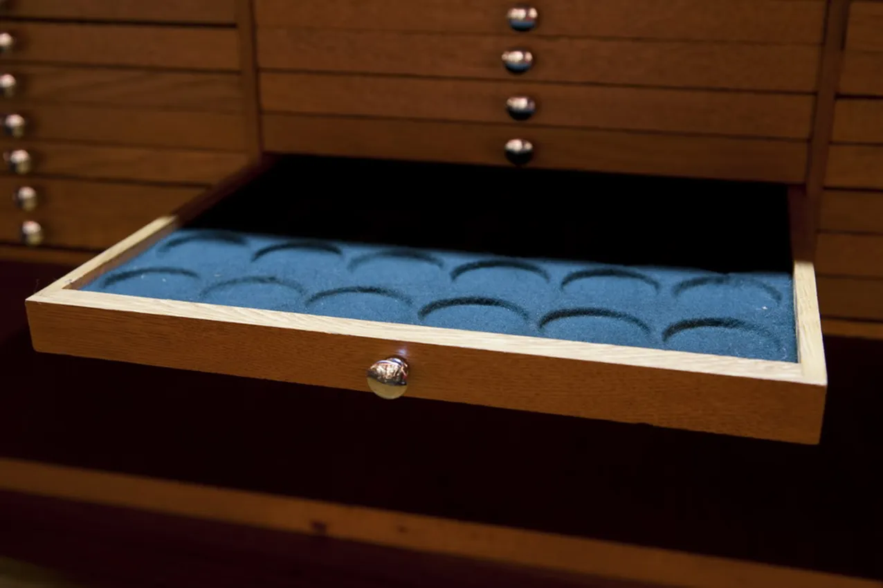 Armário antigo com compartimentos para moedas, fundo azul.