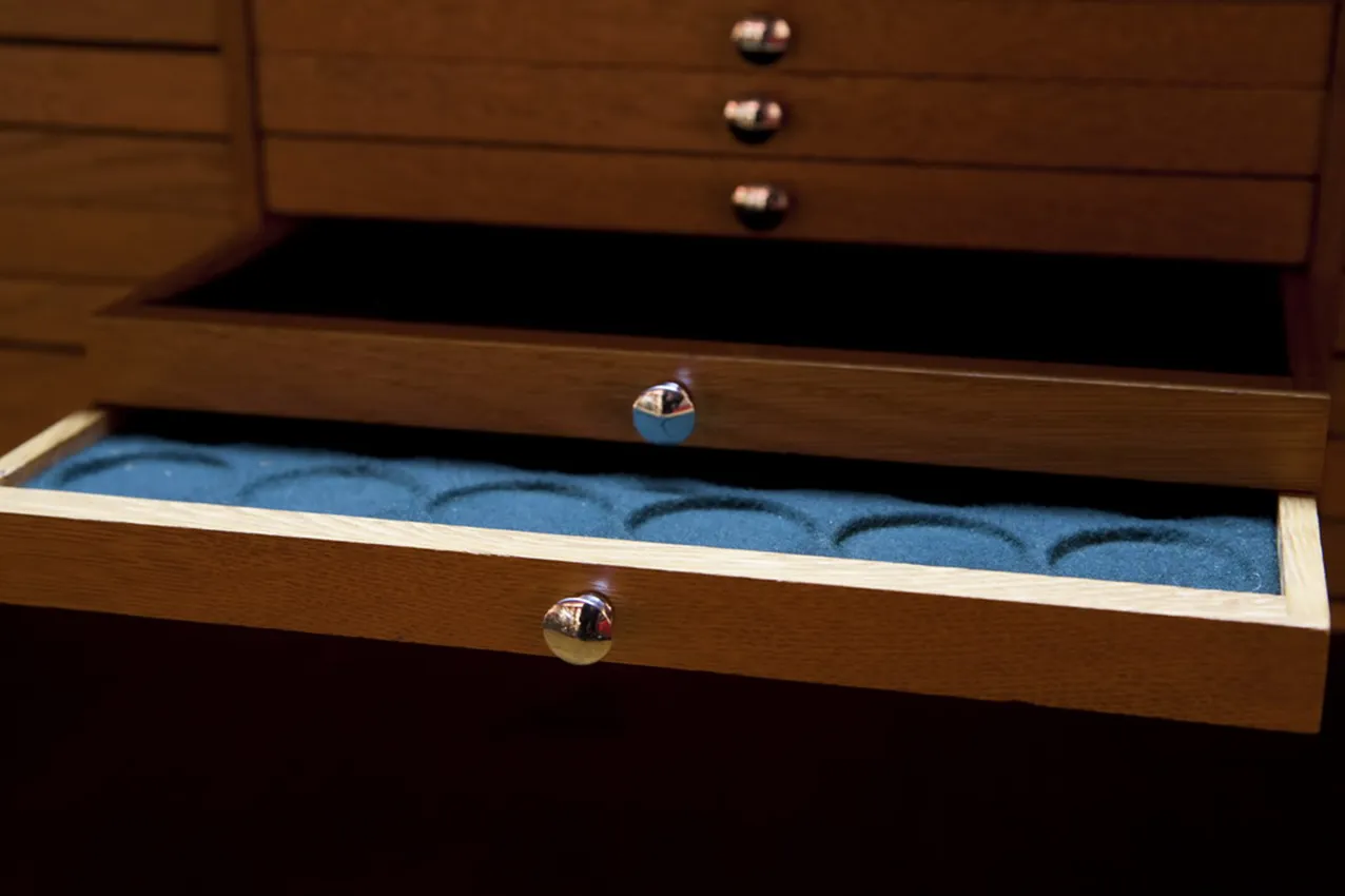 Vista de un mueble antiguo para monedas con compartimentos internos en un entorno oscuro.