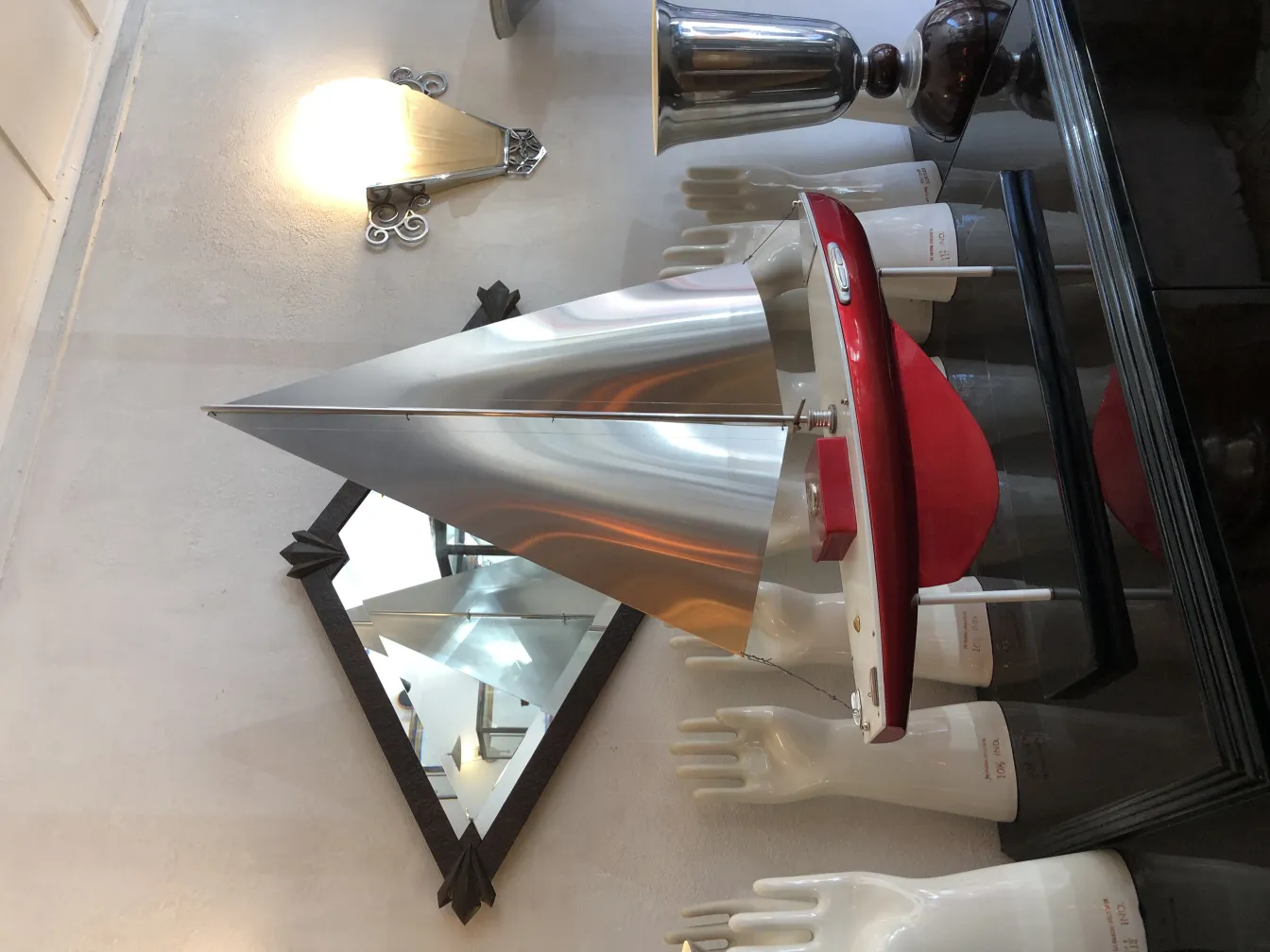 Antique decorative ship by designer Marcelo Peña with cone-shaped sail and red base in an artistic setting.