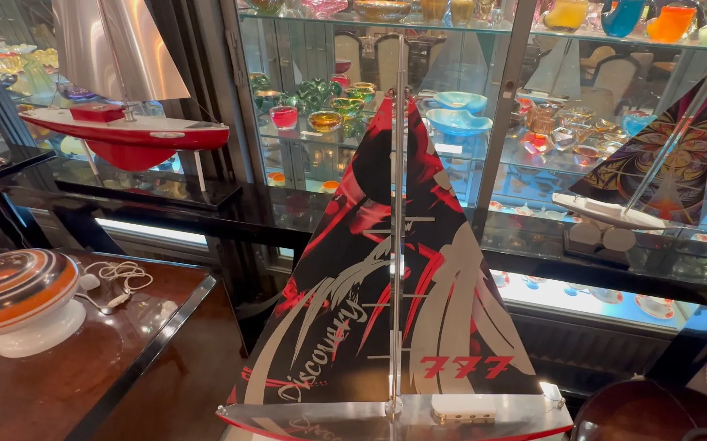 Modelo de barco del diseñador con velas rojas y diseño moderno, en un ambiente de antigüedades.