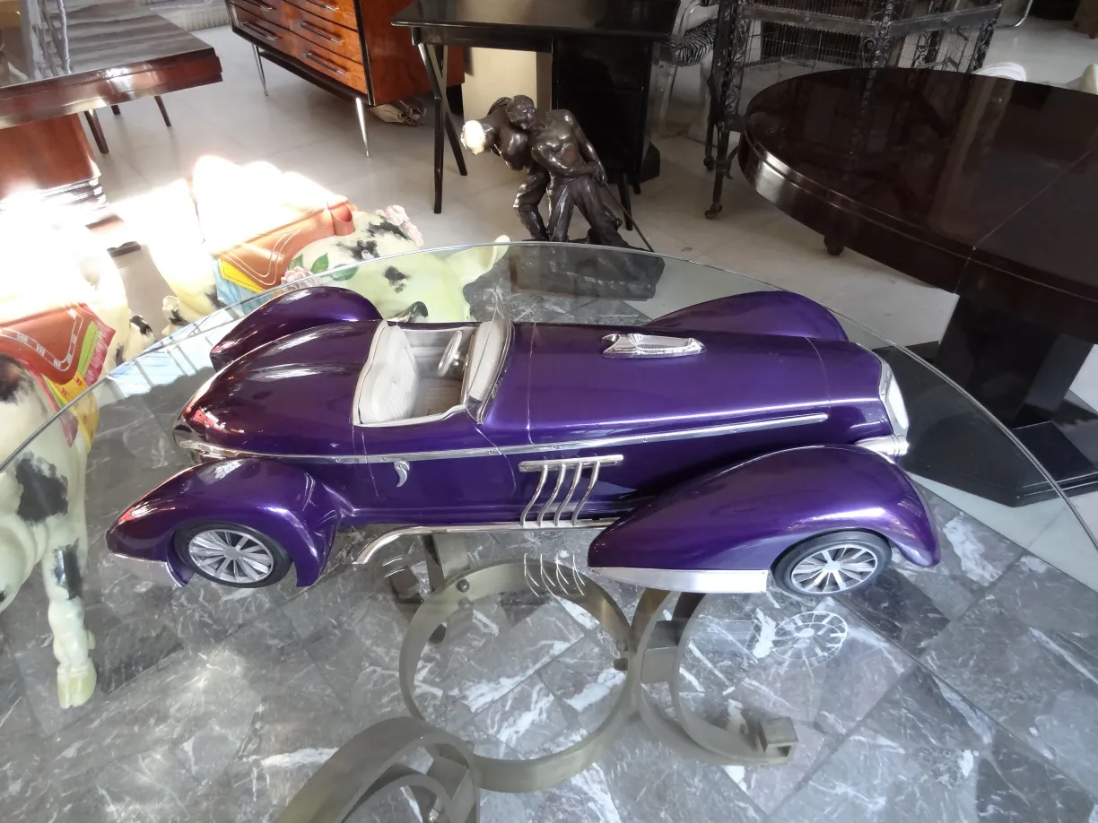 Voiture antique de designer en violet, présentant des détails raffinés. Située dans un environnement élégant avec d'autres objets de collection.