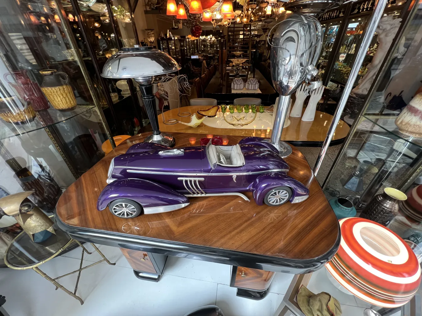 antique car model designed by Marcelo Peña, purple color, displayed in a vintage setting with lamps and decorative items.