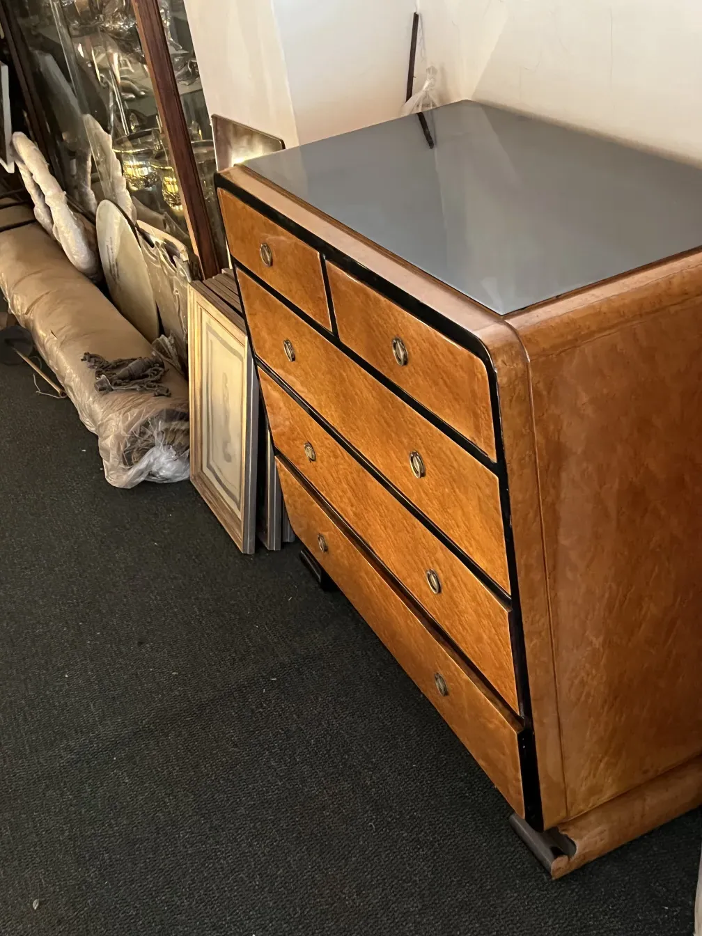 Commode antique avec des détails ornementaux et des poignées brillantes, dans un cadre avec d'autres objets décoratifs.