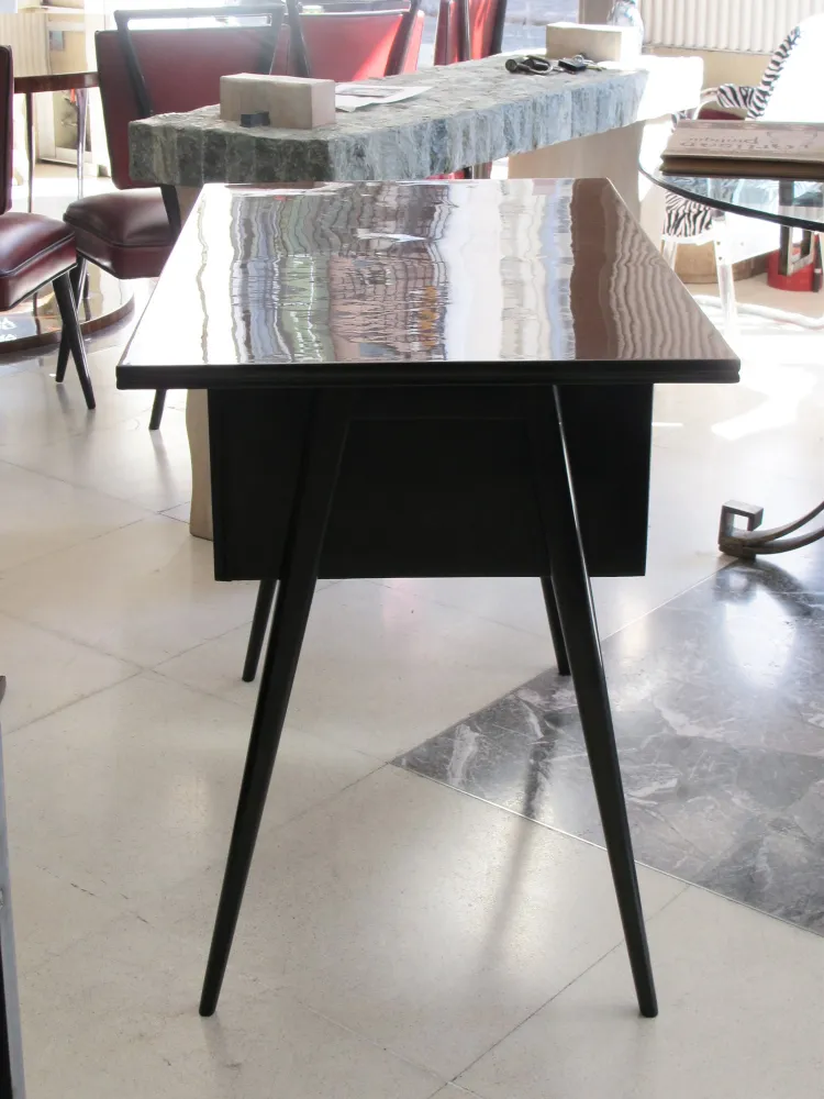 Scrivania antica con gambe sottili e design semplice in un ambiente luminoso.