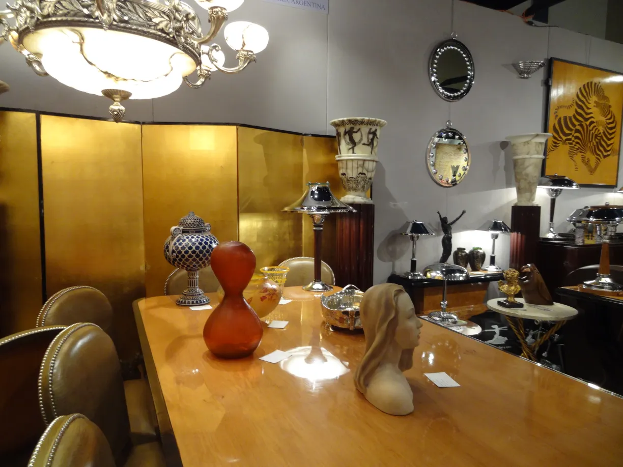 Lampe de bureau ancienne avec une base et un abat-jour décoratifs, entourée d'autres objets dans un cadre élégant.