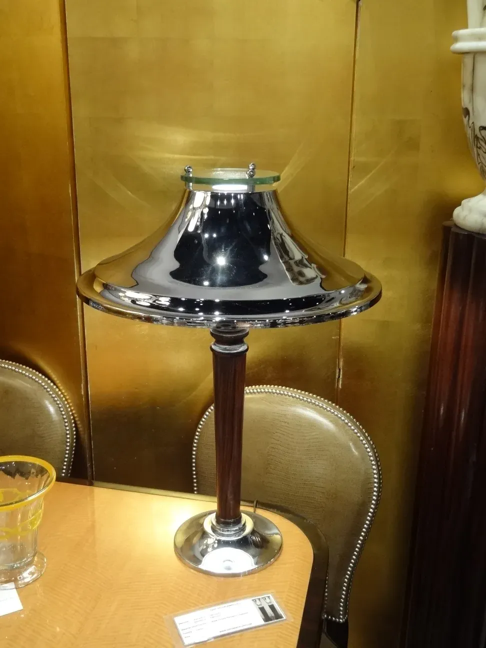 Luminária de mesa antiga com base brilhante e detalhes elegantes. Fundo dourado e ambiente clássico.