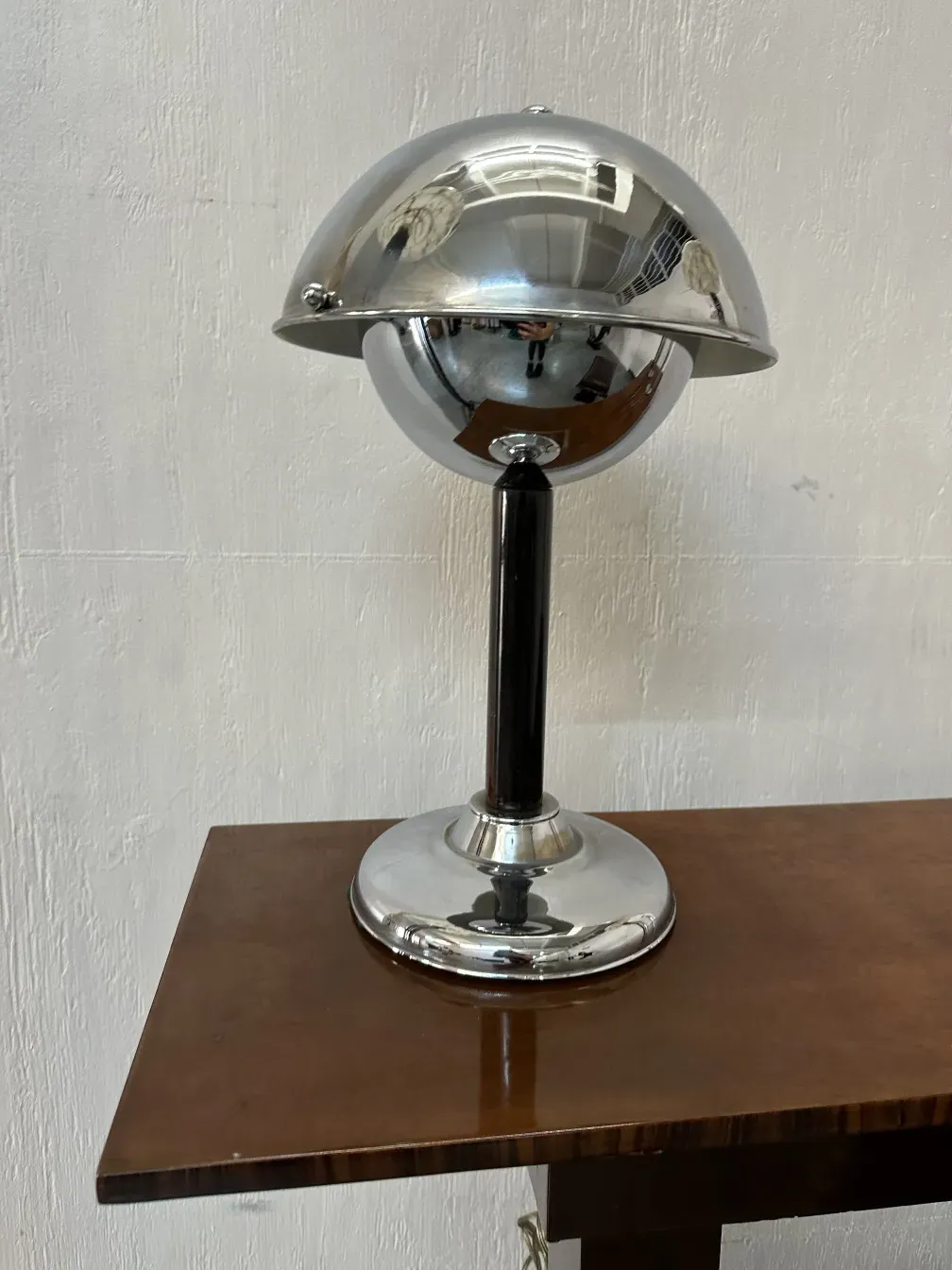 Lampada da tavolo antica con design sferico lucido e elegante supporto nero, posizionata su un tavolo di legno.