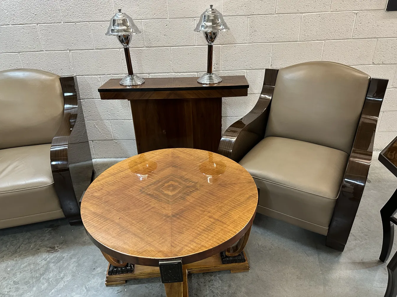 Conjunto de 2 poltronas antigas em um ambiente acolhedor, com lâmpadas e uma mesa redonda, todos em cores neutras.